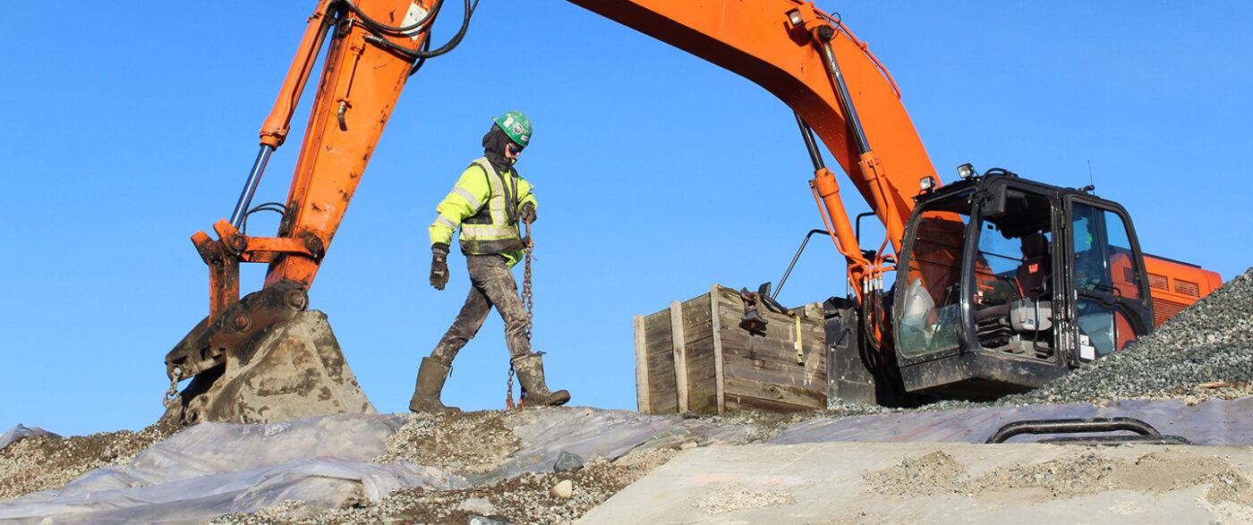 Construction worker walking by orange hitachi excavator